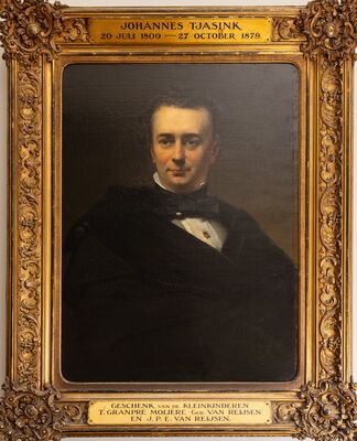 Geschilderd portret van een man met een zwarte strik om zijn hoge witte boord, een sierspeld op zijn overhemd en een donkere mantel over zijn schouders, in een rijk bewerkte vergulde lijst. Op het plaatje boven de lijst: Johannes Tjasink, 20 Juli 1809 – 27 October 1879; eronder: Geschenk van de kleinkinderen T. Granpré Molière geb. van Reijsen en J.P.E. van Reijsen.