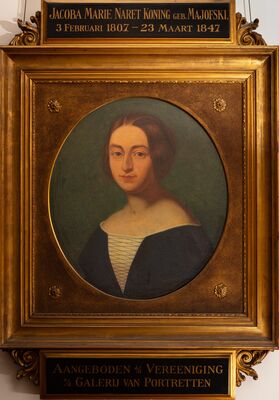 Ovaal geschilderd portret van een vrouw met gescheiden, naar achteren gekamd haar, in een donkerblauwe jurk over een lichte, met veters gesloten bovenkant, tegen een groene achtergrond. In een vergulde lijst met rozetten; boven het schilderij een plaatje met JACOBA MARIE NARET KONING geb. MAJOFSKI, 3 Februari 1807 — 23 Maart 1847, eronder: Aangeboden d/d Vereeniging v/d Galerij van Portretten.