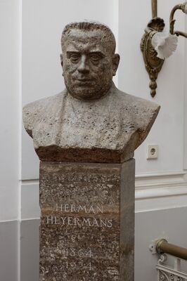 Grofgehouwen buste van grijsbruine steen: een man met kort haar en zware wenkbrauwen, frontaal. De stenen sokkel draagt de inscriptie HERMAN HEYERMANS 1864-1924. Rechts aan de wand een messing wandlamp.