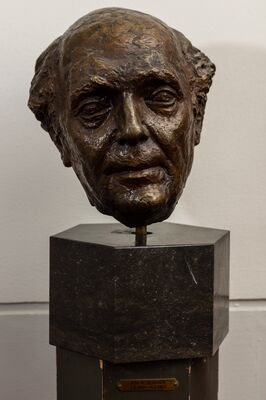 Bronzen kop van een oudere man met een smal, ingevallen gezicht en dun haar, op een donkere stenen sokkel. Op het messing plaatje eronder: JOH. M BENDIEN, 7.6.1891 – 14.9.1963.