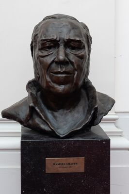 Bronzen buste van een man met een doorgroefd gezicht en een openstaande kraag, op een donkere sokkel. Op het messing plaatje: Ramses Shaffy, Jeroen Spijker – 2007.