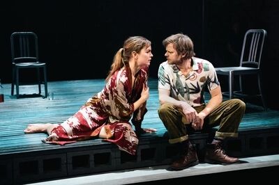Twee spelers zitten dicht bij elkaar op een houten vlonder in A Streetcar Named Desire, naar elkaar toe gedraaid; Sanne den Hartogh draagt een bedrukt shirt, zijn tegenspeelster een gebloemde kimono.