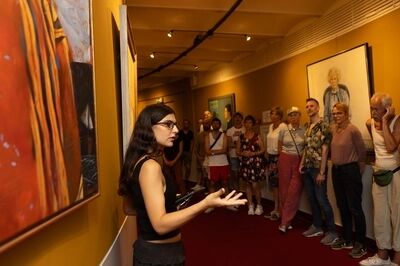 Een gids vertelt aan een groep bezoekers in de foyer tijdens de Openbare rondleiding met het Amsterdam Museum; achter hen hangen geschilderde portretten aan een gele wand.