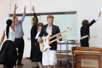 Mensen dansen met hun handen in de lucht en een man speelt gitaar.