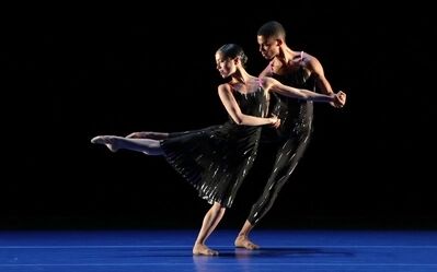 Beeld bij Nederlands Balletgala: twee dansers in zwarte kostuums op een blauw verlichte vloer. De danseres strekt haar been naar achteren terwijl de danser achter haar haar arm vasthoudt.
