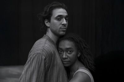 Zwart-witbeeld bij Een tijd van liefde: een man staat achter een vrouw die haar hoofd tegen zijn borst legt; beiden kijken in de camera, tegen een donkere achtergrond.