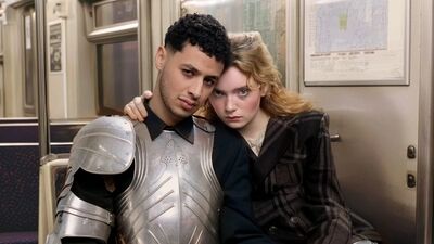 Campagnebeeld voor Romeo en Julia: twee jonge spelers zitten dicht tegen elkaar in een metrostel. Hij draagt een zilveren harnas over een zwart overhemd, zij een geruite jas en legt haar hand op zijn schouder; achter hen hangt een plattegrond.