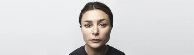 Campagnebeeld voor Mary Jane: een portret in close-up van een vrouw met naar achteren gebonden haar en een zwart shirt, die met neutrale blik recht in de camera kijkt tegen een witte achtergrond.